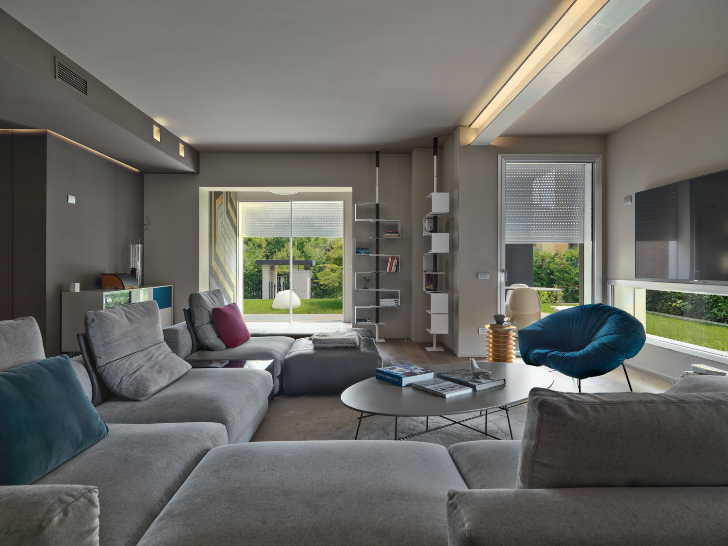 Interno di moderno soggiorno con divano in tessuto e poltroncine colorate affacciato sul giardino